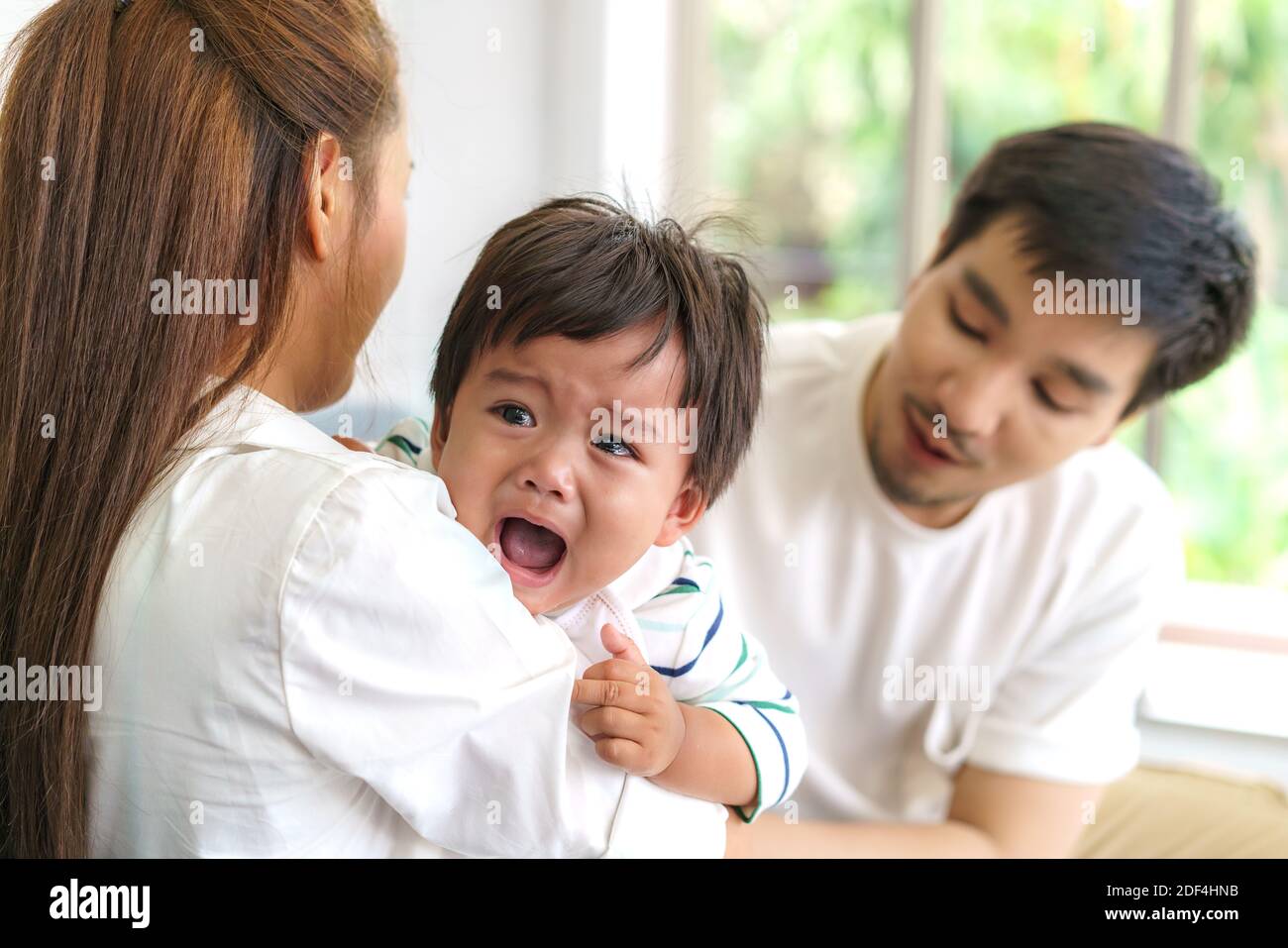 Genitori asiatici con madre e padre che cercano di calmarsi piangendo figlio infante in soggiorno a casa Foto Stock