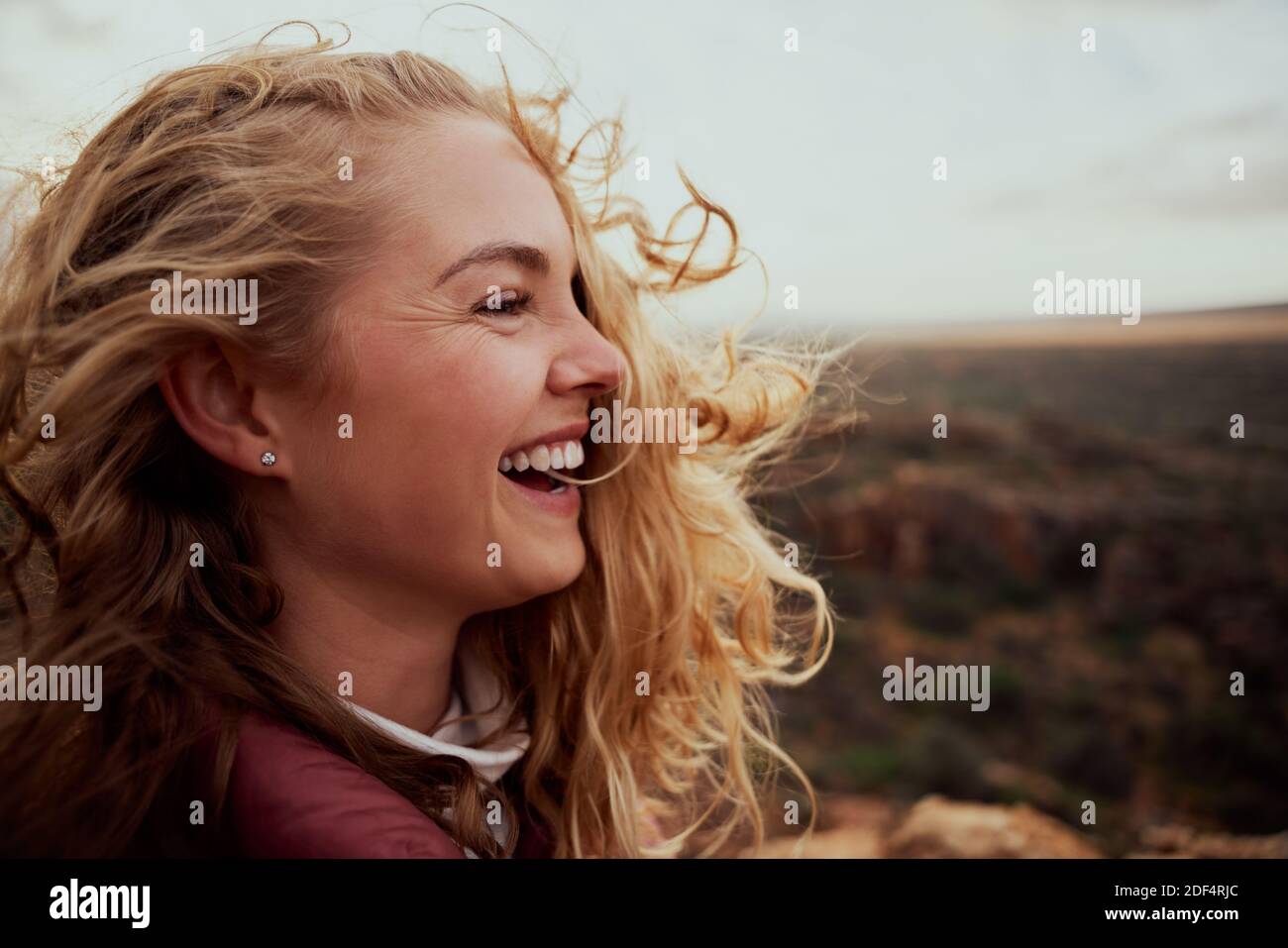 Primo piano di una giovane donna ridente che si gode ventosa brezza toccare faccia con i capelli che volano mentre osservano via - la sensibilità della libertà in natura Foto Stock