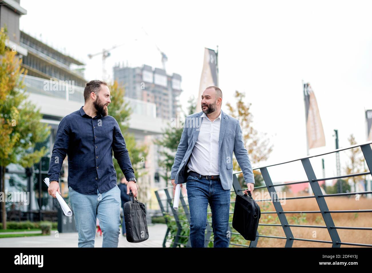 Colleghi aziendali soddisfatti che discutono del progetto sul loro cammino verso l'ufficio. Uomini d'affari che camminano fuori, tengono i documenti, parlano, ridendo. Foto Stock