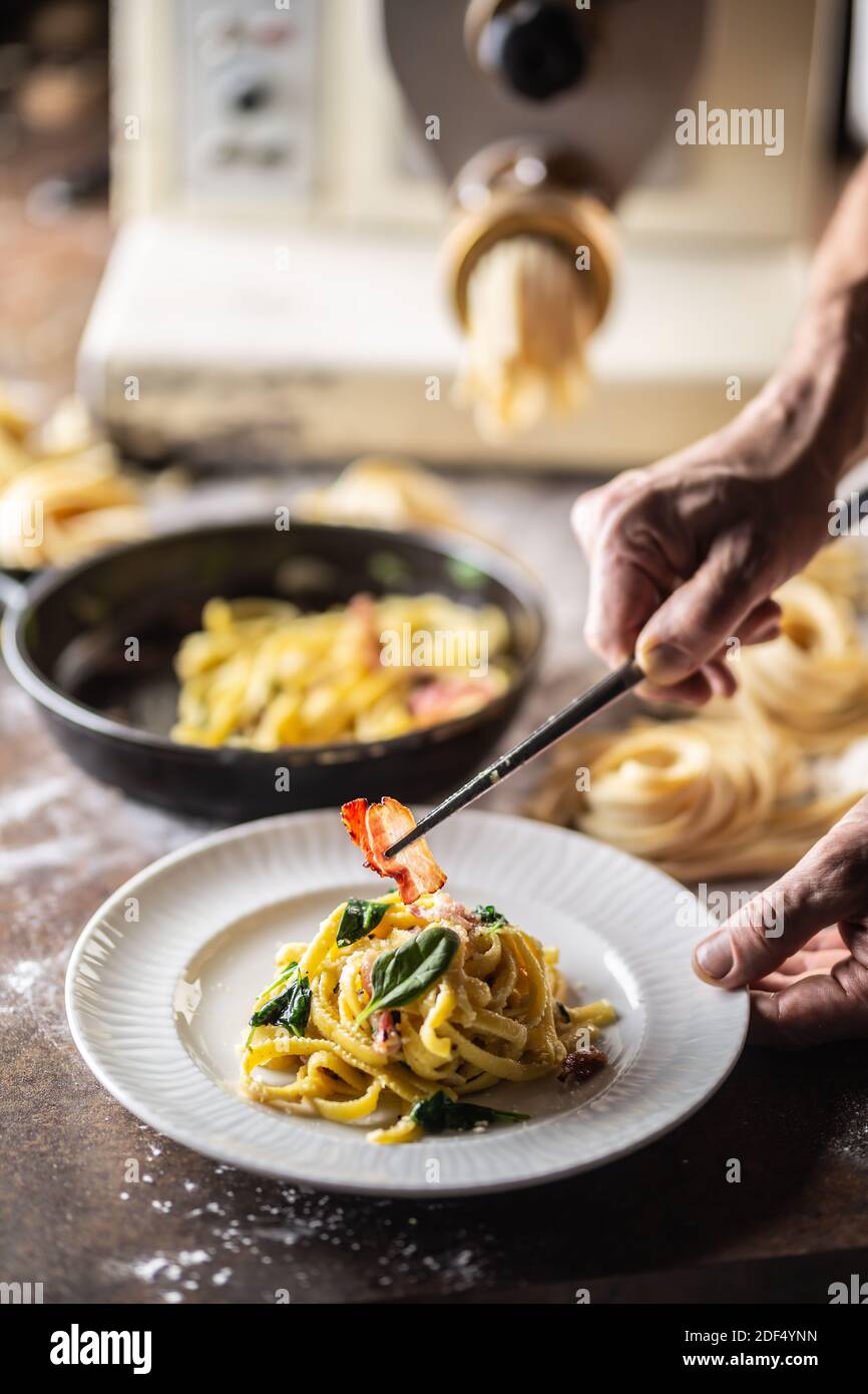 Mani di chef che cucinano pasta appena cotta con un pastificio sullo sfondo. Foto Stock