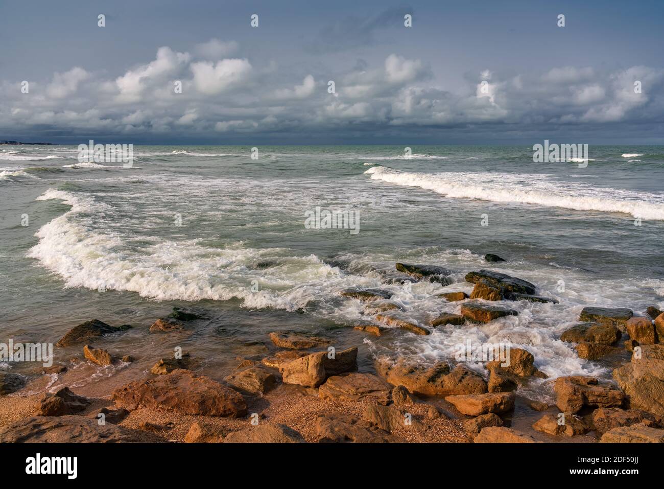 Spiaggia rocciosa vuota e mare tempestoso in tempo nuvoloso Foto Stock
