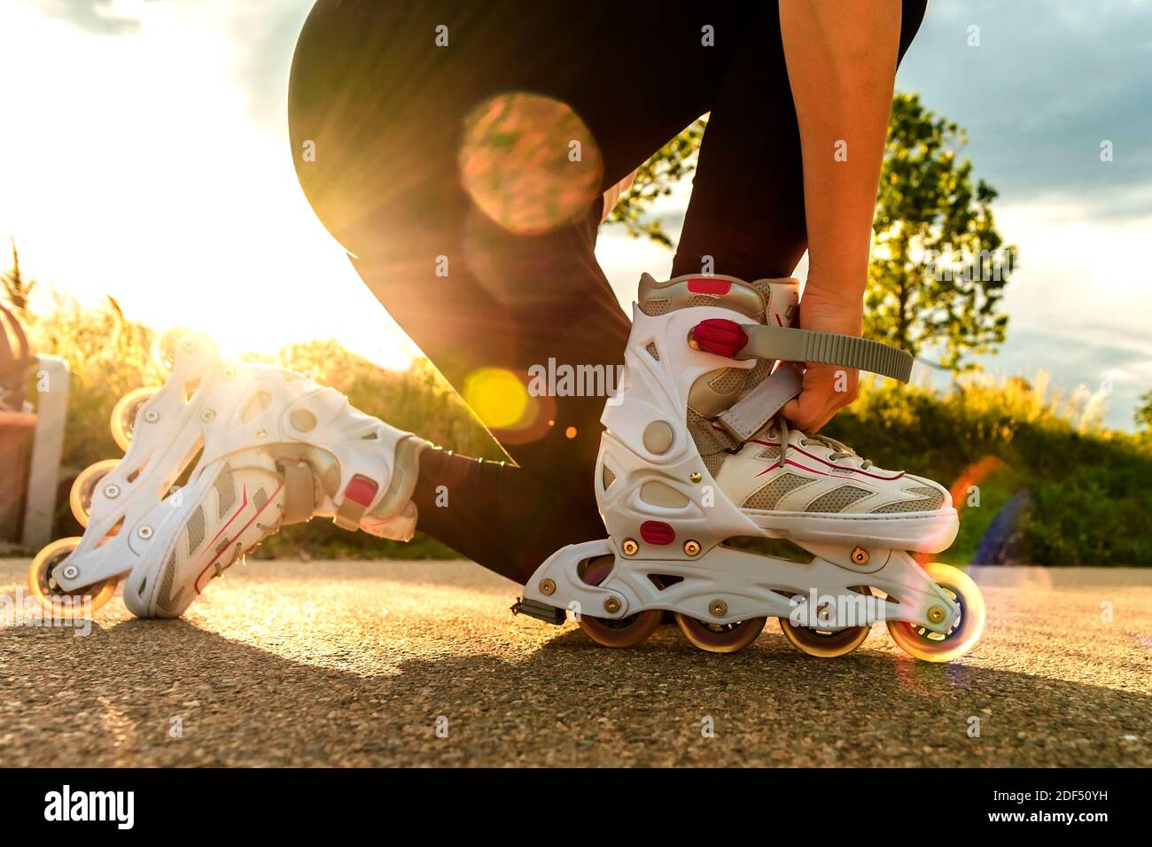 Una donna tensiona i pattini a rotelle sul percorso. Gambe donna con lame a rullo in giornata di sole. Foto Stock