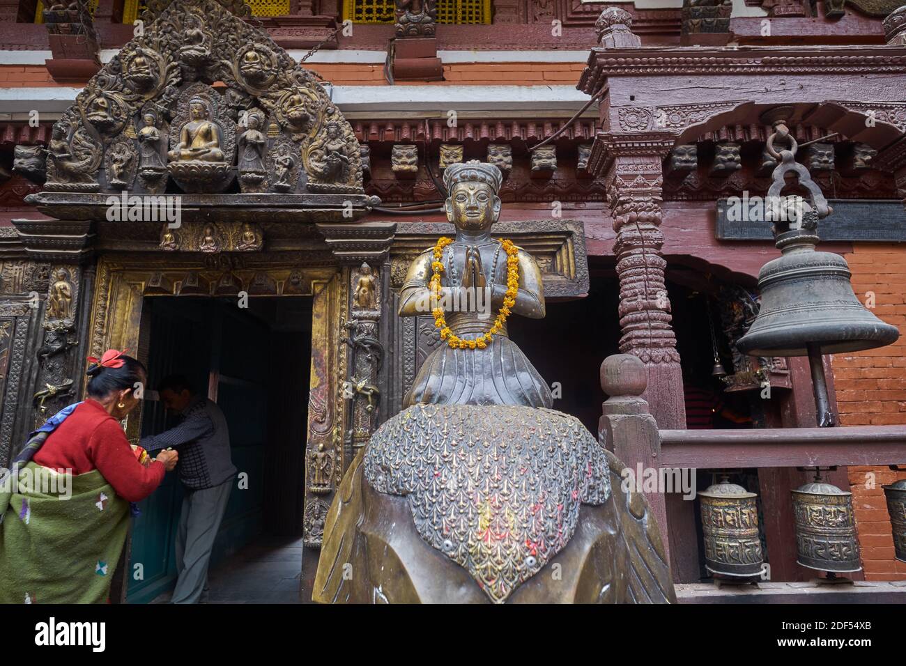Una donna lascia il cortile di Hiranya Varna Mahavihar (Kwa Bahal, Tempio d'oro), Patan (Lalitpur), Nepal, accanto a una figura di ottone di un ex re Foto Stock