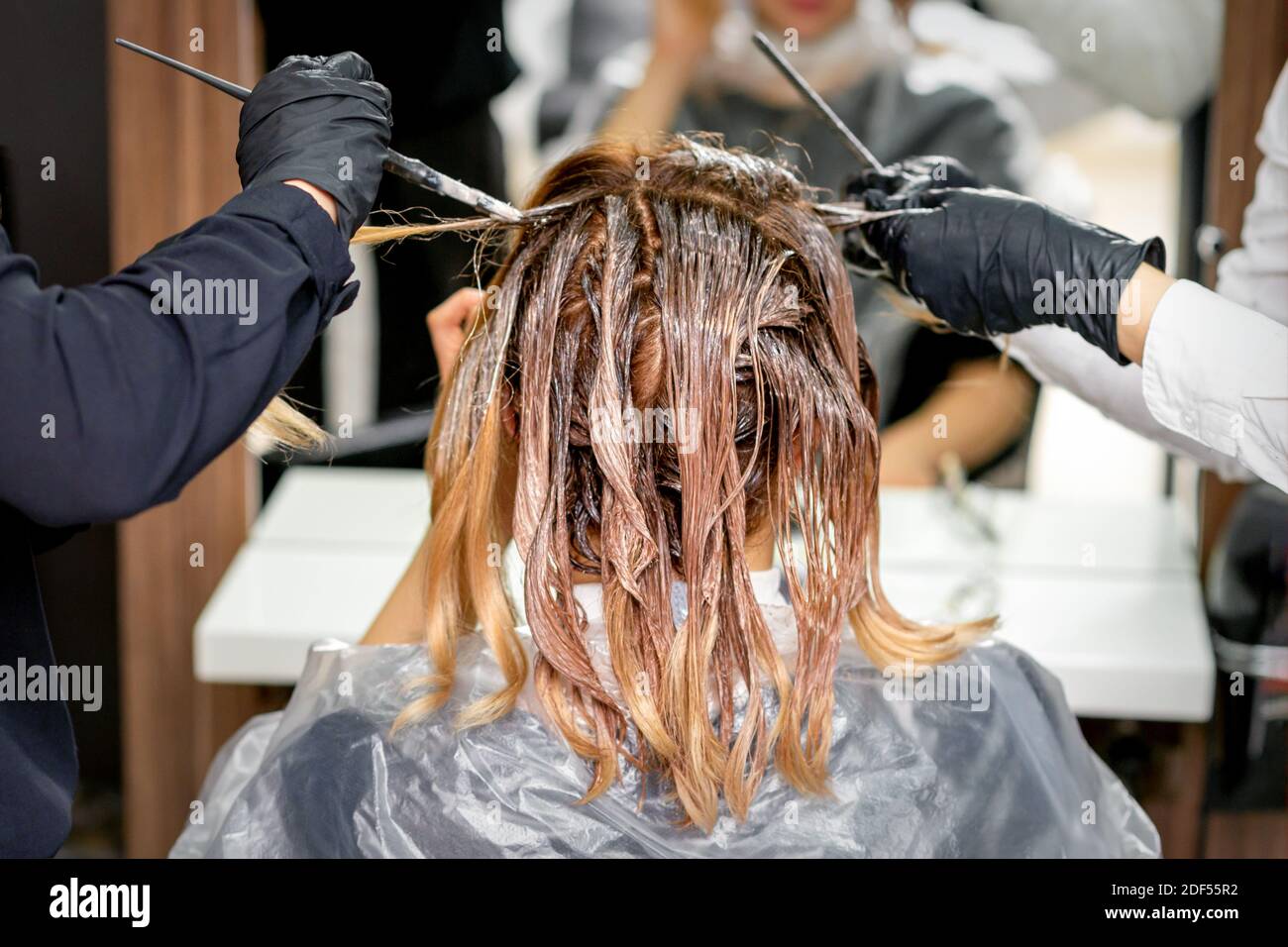 Due delle mani del parrucchiere colorano i capelli femminili con un spazzola in un parrucchiere Foto Stock
