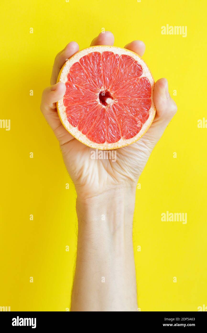 Mano che tiene mezzo pompelmo su sfondo giallo con spazio di copia Foto Stock