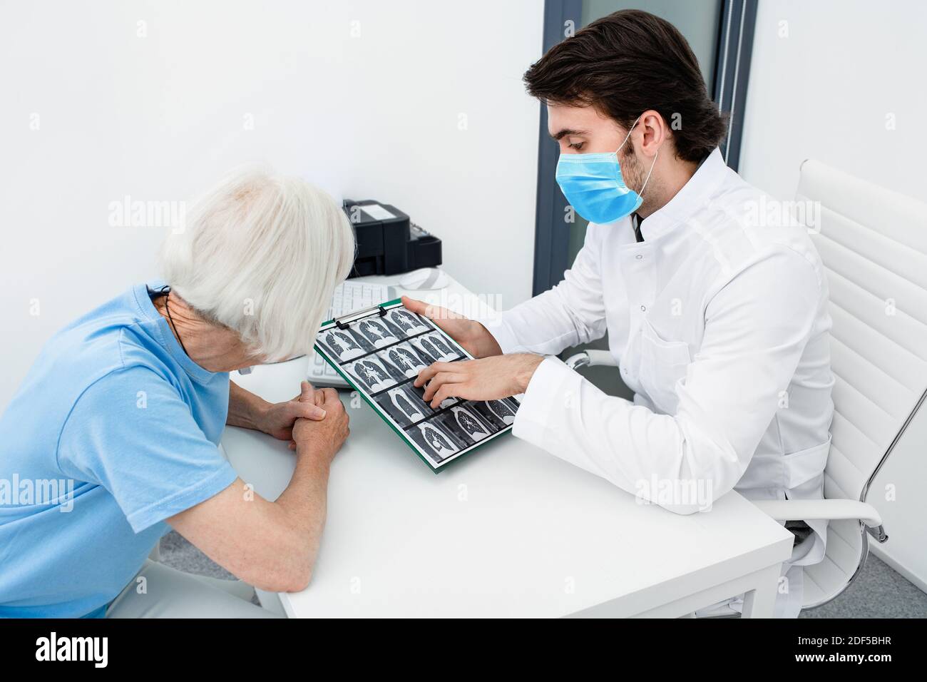 Pulmonologa indossando una maschera chirurgica che mostra ad un paziente anziano una scansione TC dei suoi polmoni. Polmonite, coronavirus, malattie polmonari Foto Stock