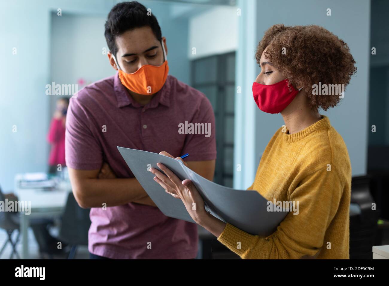 Razza mista uomo e donna che indossa maschere in un ufficio Foto Stock