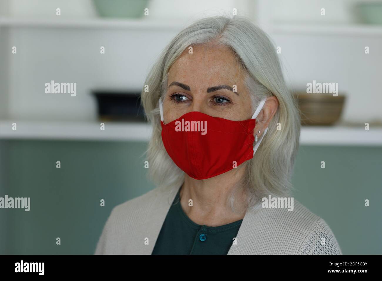 Donna caucasica anziana che indossa la maschera facciale a casa Foto Stock
