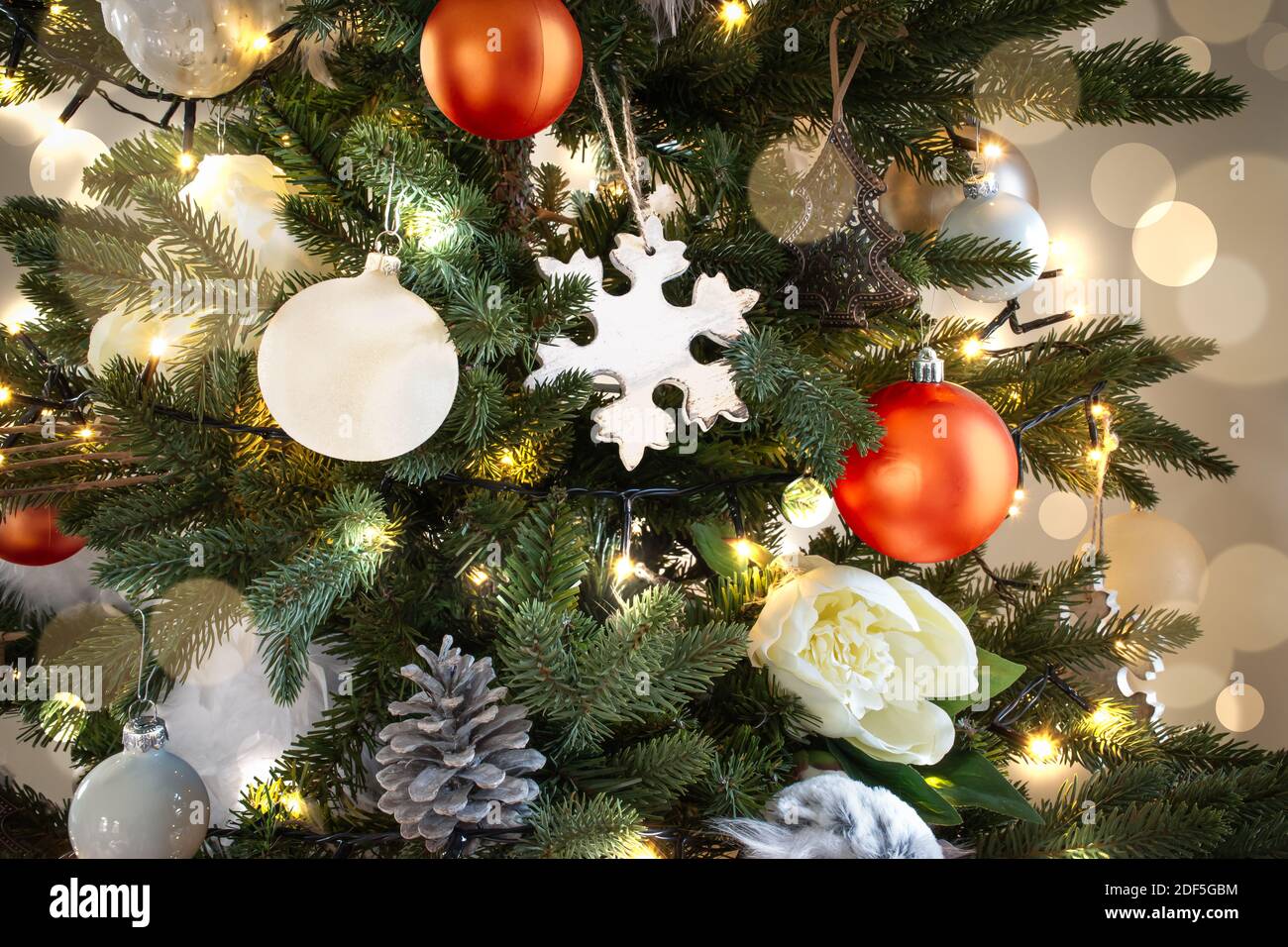 Albero di Natale illuminato con decorazioni natalizie bianche e arancioni e luce svasata. Foto Stock