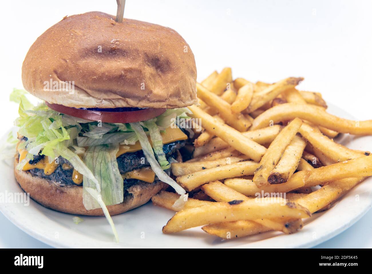 Cheeseburger doppio impilato con lattuga, pomodoro, servito con patatine fritte per deliziare le papille gustative. Foto Stock