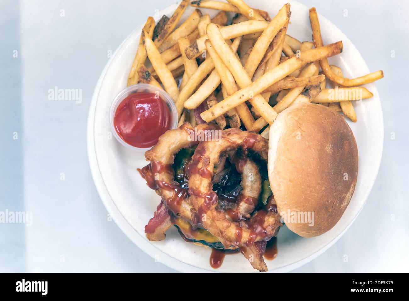 Vista dall'alto di enormi anelli di cipolle sgocciolati con salsa al barbecue su hamburger serviti con patatine fritte e salsa da immersione. Foto Stock
