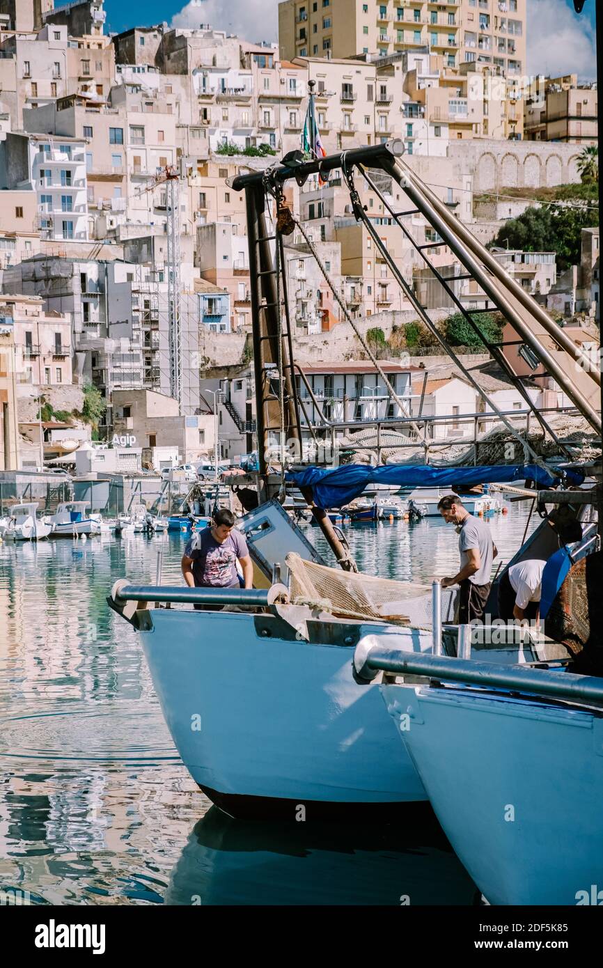 Sciacca Sicilia ottobre 2020, barche da pesca e persone riparano reti nella colorata città di Sciacca che si affaccia sul suo porto. Provincia di Agrigento, Sicilia. Foto di alta qualità Foto Stock