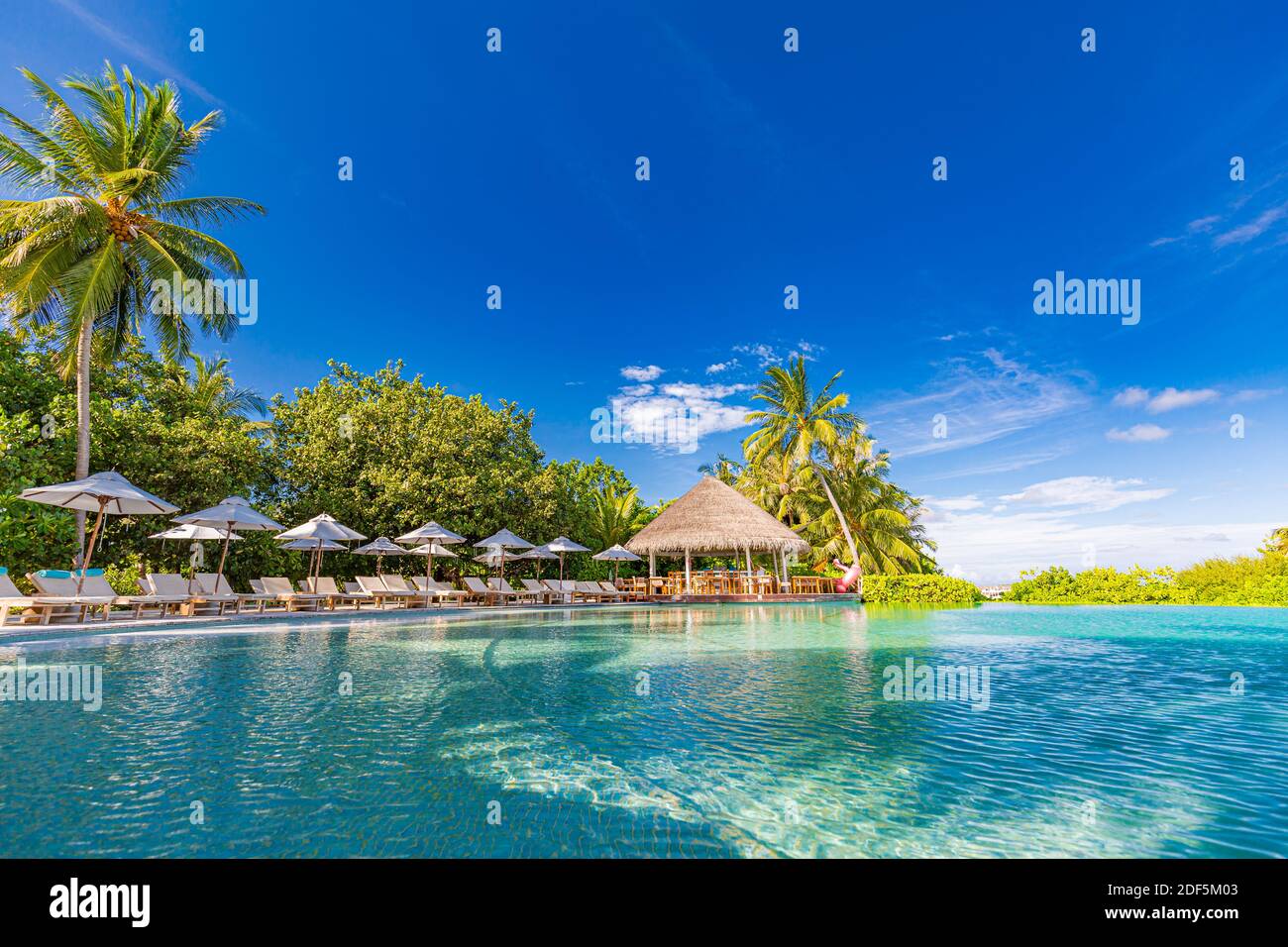 paesaggio turistico. Lussuoso resort sulla spiaggia con piscina e sedie a sdraio o lettini sotto ombrelloni con palme e cielo blu. Isola estiva Foto Stock