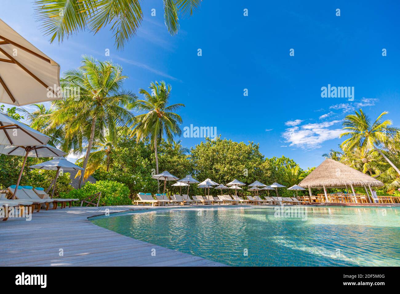 paesaggio turistico. Lussuoso resort sulla spiaggia con piscina e sedie a sdraio o lettini sotto ombrelloni con palme e cielo blu. Isola estiva Foto Stock