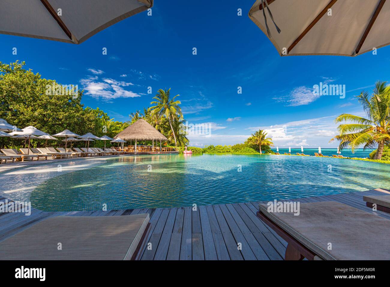 paesaggio turistico. Lussuoso resort sulla spiaggia con piscina e sedie a sdraio o lettini sotto ombrelloni con palme e cielo blu. Isola estiva Foto Stock