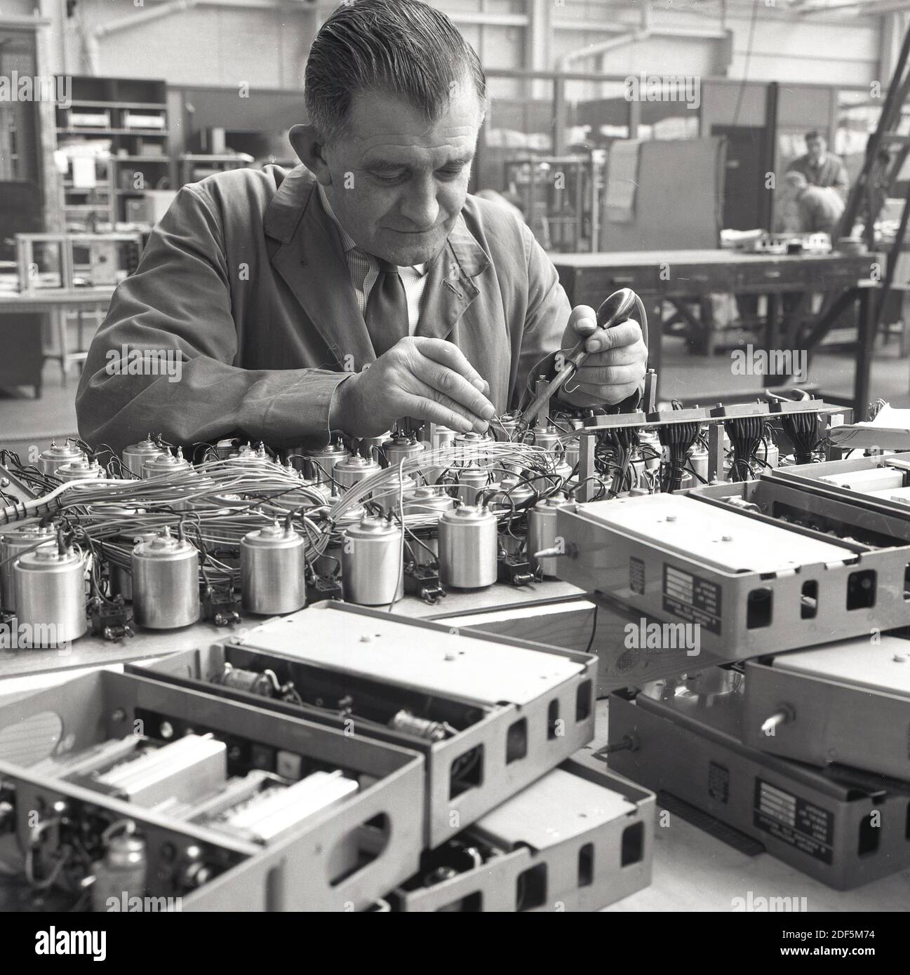 anni '1950, storico, un abile tecnico aeronautico che lavora su componenti elettrici di aeromobili utilizzando uno strumento di saldatura per unire due fili. Foto Stock