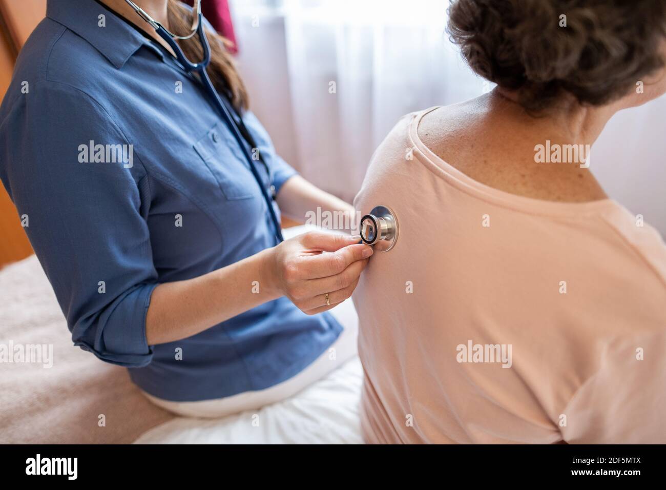 Vista ritagliata dello stetoscopio per inserimento infermieri sul retro di pazienti anziani di sesso femminile nella stanza dell'ospedale. Foto Stock