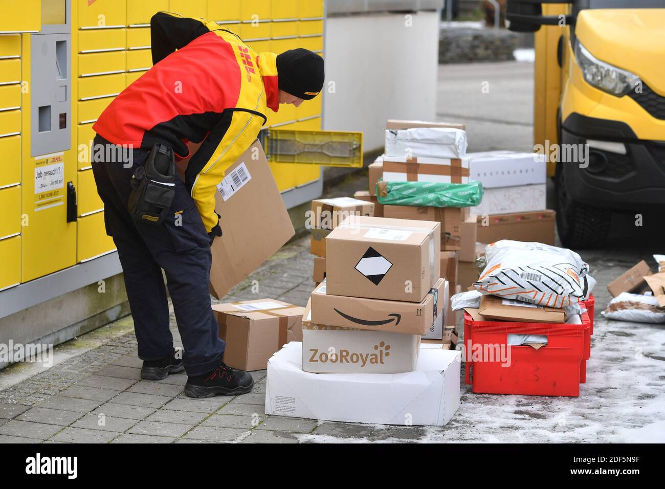 Monaco, Germania. 03 dic 2020. I volumi dei pacchi e il commercio online stanno fiorendo in tempi di pandemia del virus della corona. DHL spedizioniere, spedizioniere, al lavoro mette il pacco in un compartimento di una stazione di imballaggio. Scarica la sua vettura di pacco, il bus postale, DHL, pacco, pacchi, servizio di pacco, consegna, consegna, scarico, spedizione, trasportatore, camion a mano. | utilizzo in tutto il mondo credito: dpa/Alamy Live News Foto Stock