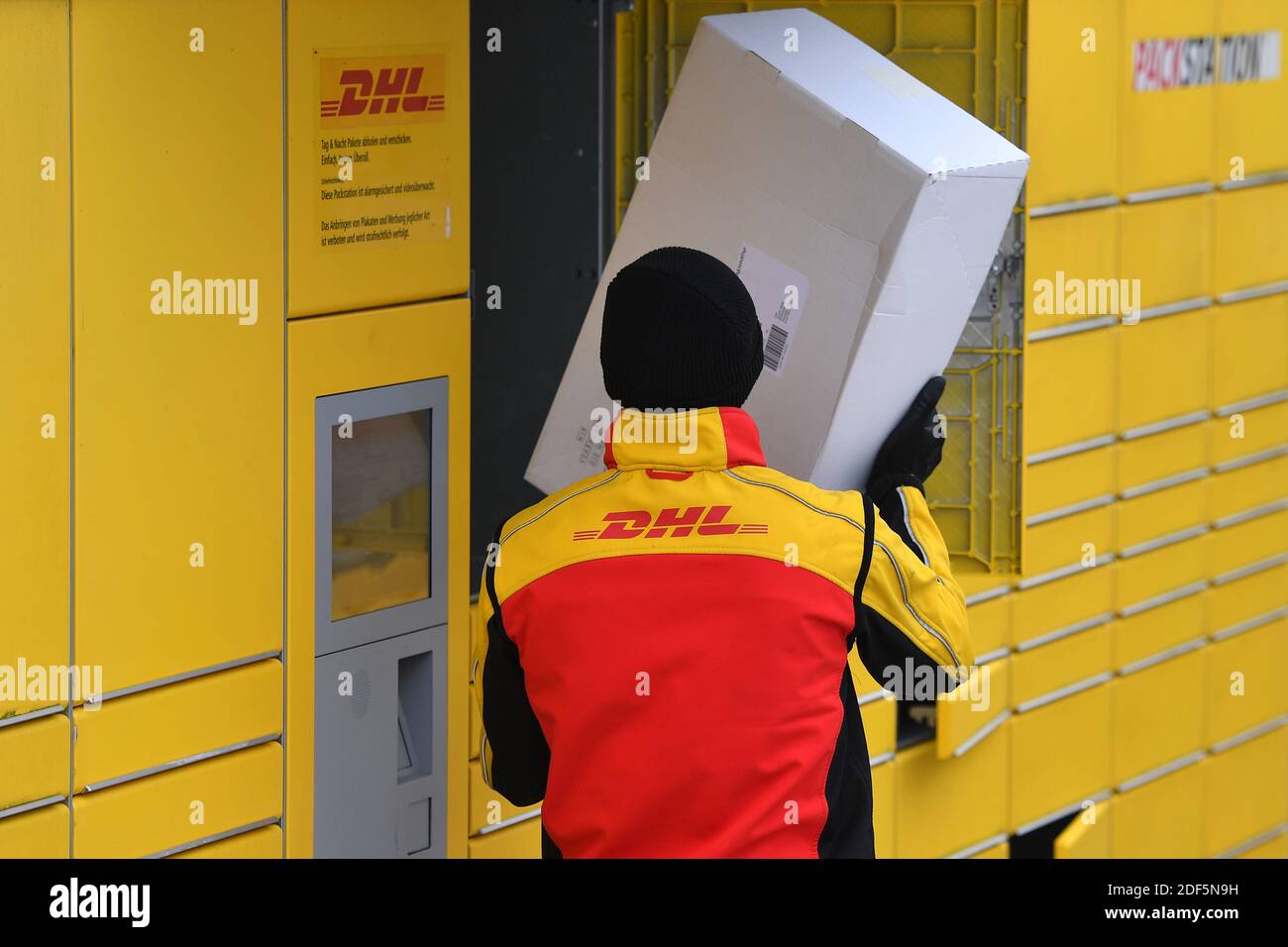 Monaco, Germania. 03 dic 2020. I volumi dei pacchi e il commercio online stanno fiorendo in tempi di pandemia del virus della corona. DHL spedizioniere, spedizioniere, al lavoro mette il pacco in un compartimento di una stazione di imballaggio. Scarica la sua vettura di pacco, il bus postale, DHL, pacco, pacchi, servizio di pacco, consegna, consegna, scarico, spedizione, trasportatore, camion a mano. | utilizzo in tutto il mondo credito: dpa/Alamy Live News Foto Stock