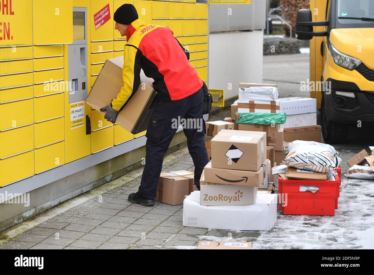 Monaco, Germania. 03 dic 2020. I volumi dei pacchi e il commercio online stanno fiorendo in tempi di pandemia del virus della corona. DHL spedizioniere, spedizioniere, al lavoro mette il pacco in un compartimento di una stazione di imballaggio. Scarica la sua vettura di pacco, il bus postale, DHL, pacco, pacchi, servizio di pacco, consegna, consegna, scarico, spedizione, trasportatore, camion a mano. | utilizzo in tutto il mondo credito: dpa/Alamy Live News Foto Stock