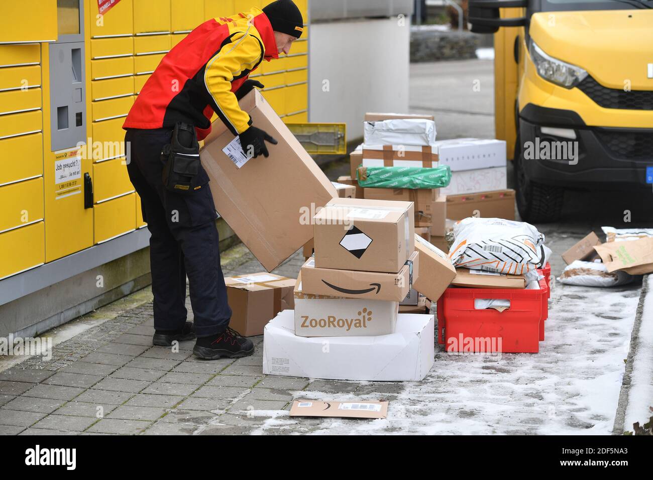 Monaco, Germania. 03 dic 2020. I volumi dei pacchi e il commercio online stanno fiorendo in tempi di pandemia del virus della corona. DHL spedizioniere, spedizioniere, al lavoro mette il pacco in un compartimento di una stazione di imballaggio. Scarica la sua vettura di pacco, il bus postale, DHL, pacco, pacchi, servizio di pacco, consegna, consegna, scarico, spedizione, trasportatore, camion a mano. | utilizzo in tutto il mondo credito: dpa/Alamy Live News Foto Stock