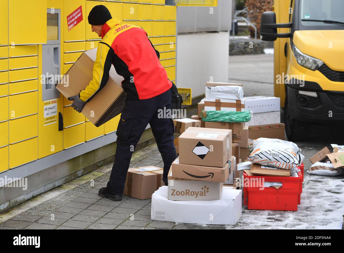 Monaco, Germania. 03 dic 2020. I volumi dei pacchi e il commercio online stanno fiorendo in tempi di pandemia del virus della corona. DHL spedizioniere, spedizioniere, al lavoro mette il pacco in un compartimento di una stazione di imballaggio. Scarica la sua vettura di pacco, il bus postale, DHL, pacco, pacchi, servizio di pacco, consegna, consegna, scarico, spedizione, trasportatore, camion a mano. | utilizzo in tutto il mondo credito: dpa/Alamy Live News Foto Stock