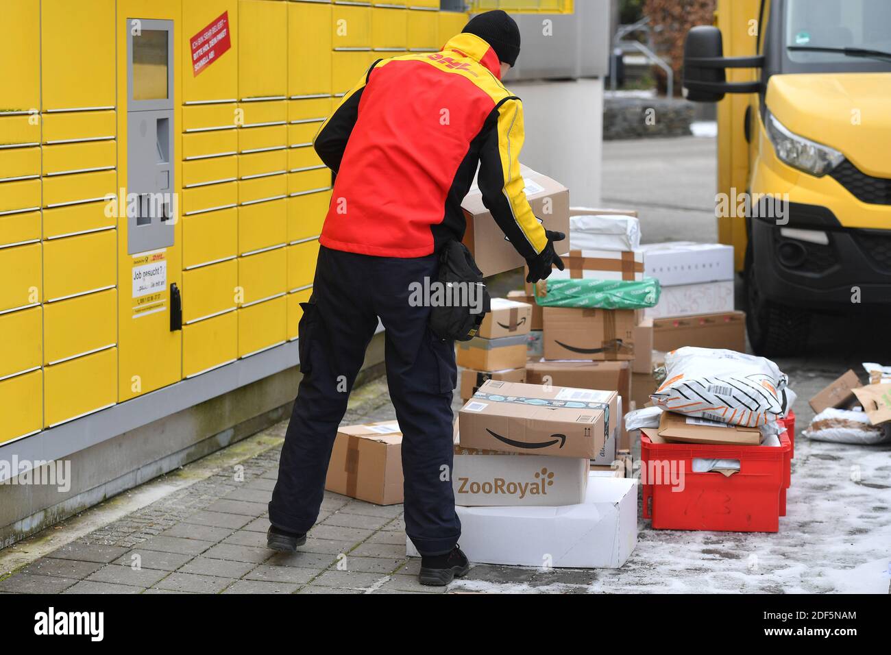 Monaco, Germania. 03 dic 2020. I volumi dei pacchi e il commercio online stanno fiorendo in tempi di pandemia del virus della corona. DHL spedizioniere, spedizioniere, al lavoro mette il pacco in un compartimento di una stazione di imballaggio. Scarica la sua vettura di pacco, il bus postale, DHL, pacco, pacchi, servizio di pacco, consegna, consegna, scarico, spedizione, trasportatore, camion a mano. | utilizzo in tutto il mondo credito: dpa/Alamy Live News Foto Stock