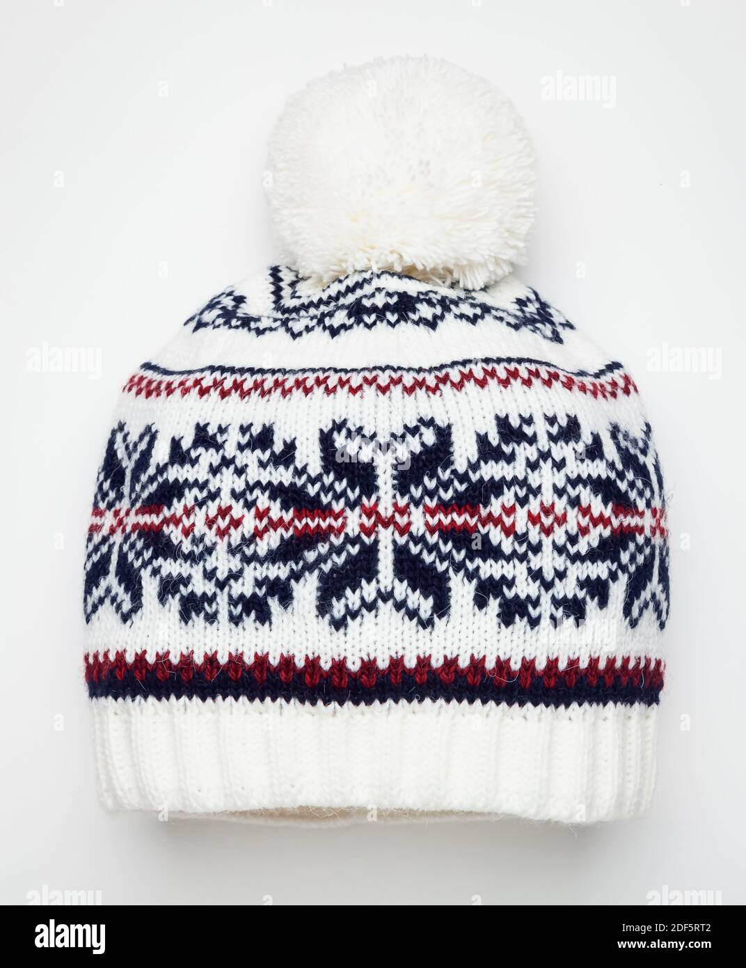 Cappellino invernale lavorato a maglia bianca decorato con ornamenti geometrici scandinavi. Cappuccio in lana fatto a mano con pompon sopra Foto Stock