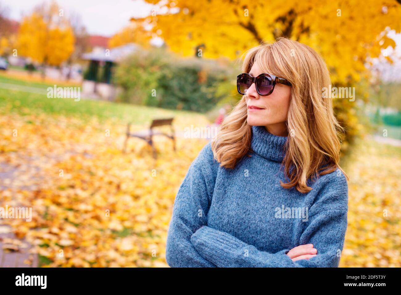 Foto ritratto di donna matura sorridente che indossa occhiali da sole e pullover a collo di turnolo mentre ti rilassi al parco in autunno. Foto Stock