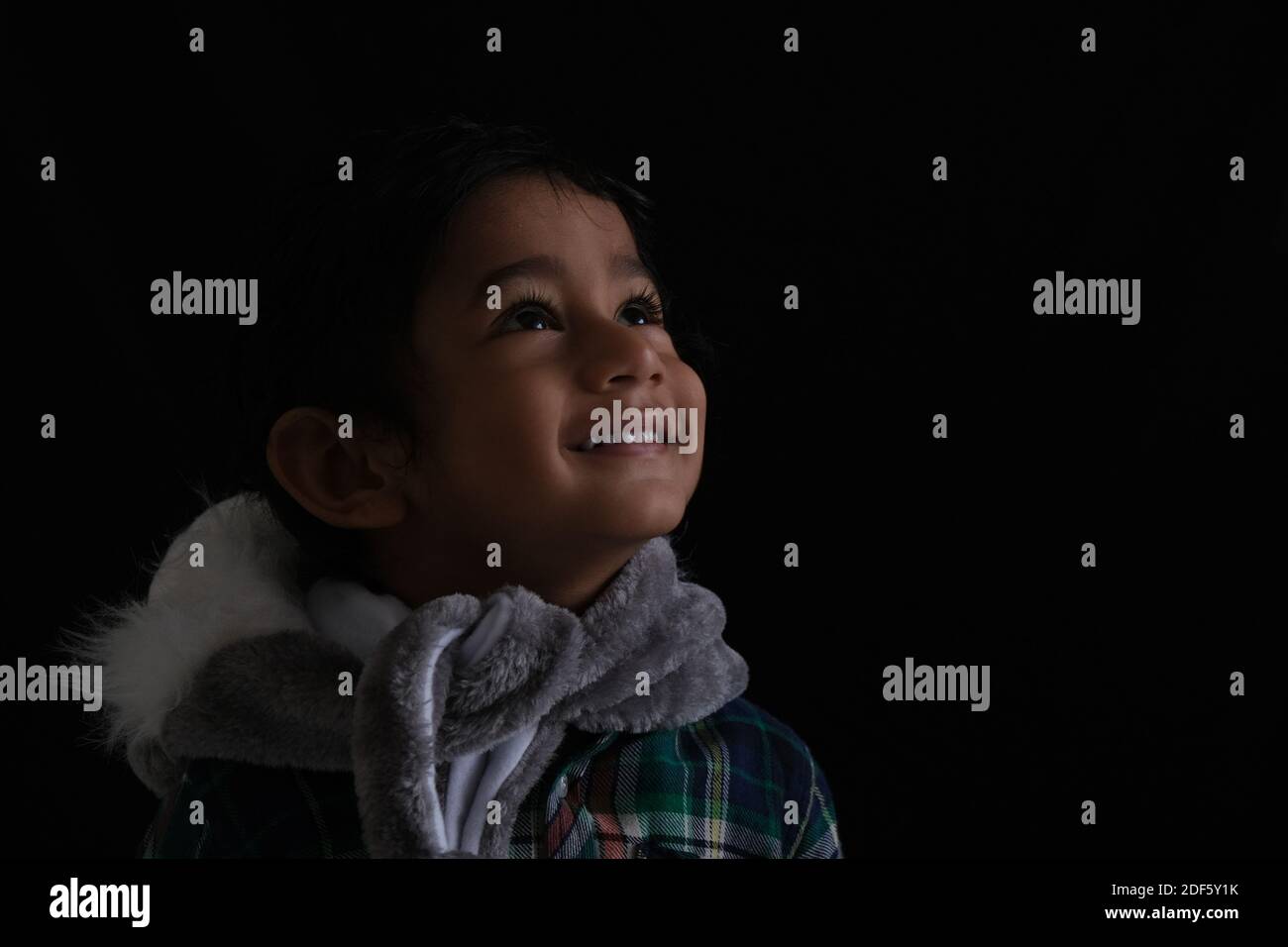 Primo piano ritratto di indiano carino bruna poco allegro Tamil baby boy che indossa un abito casual e un silenziatore di pelliccia in un sfondo nero Foto Stock