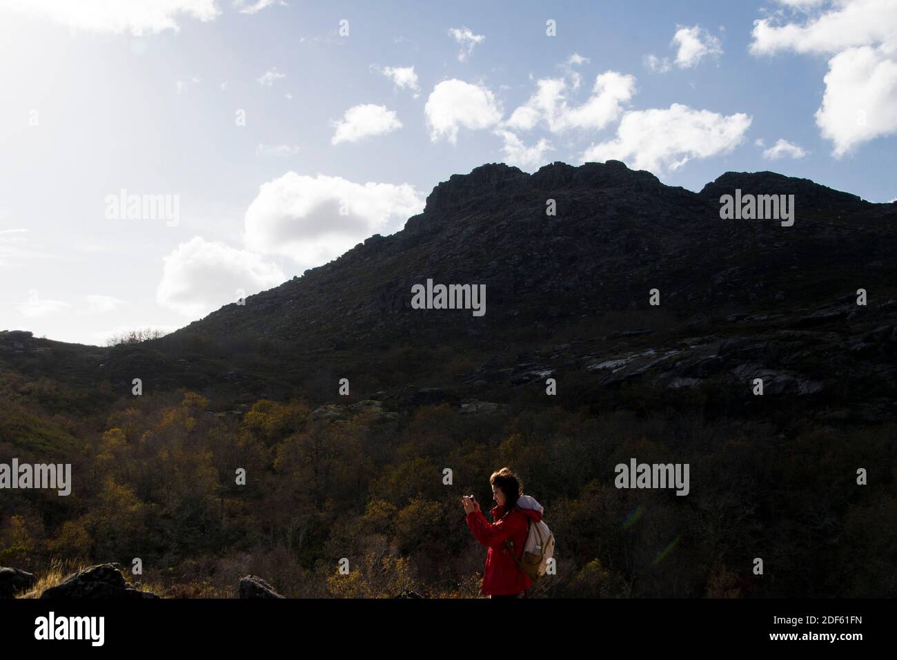 Donna si alza al sole su un paesaggio di montagna mentre si prende una foto durante un'escursione Foto Stock