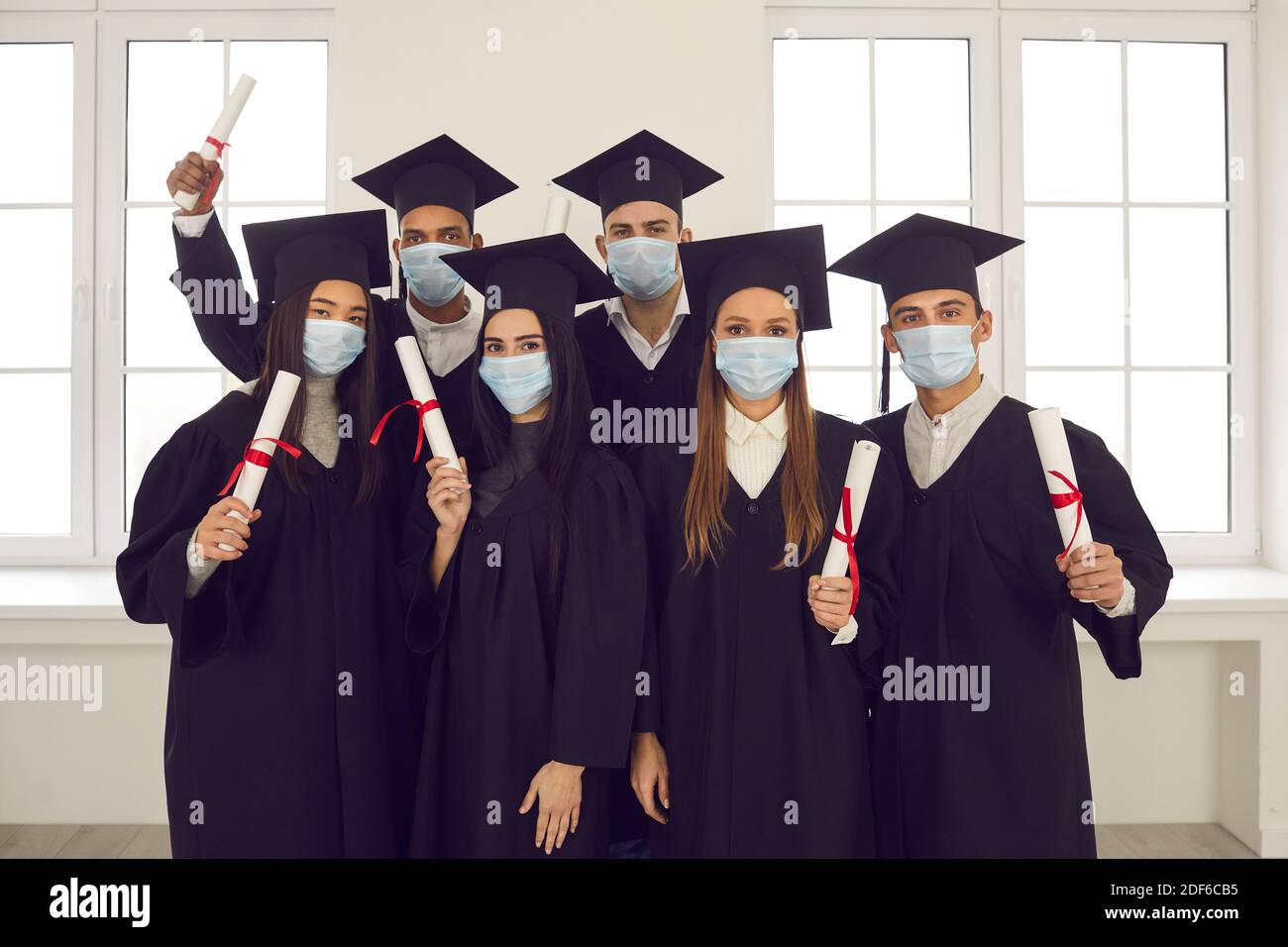 Ritratto di gruppo di laureati di razza mista in maschere di protezione i loro diplomi Foto Stock