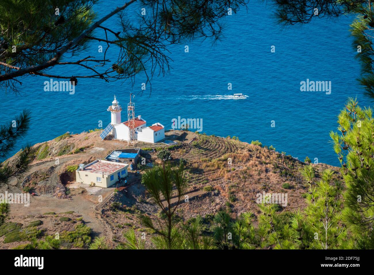 Vista dall'alto di un faro tra i verdi pini che sembrano una cornice naturale e una barca galleggiante intorno al faro. Foto Stock