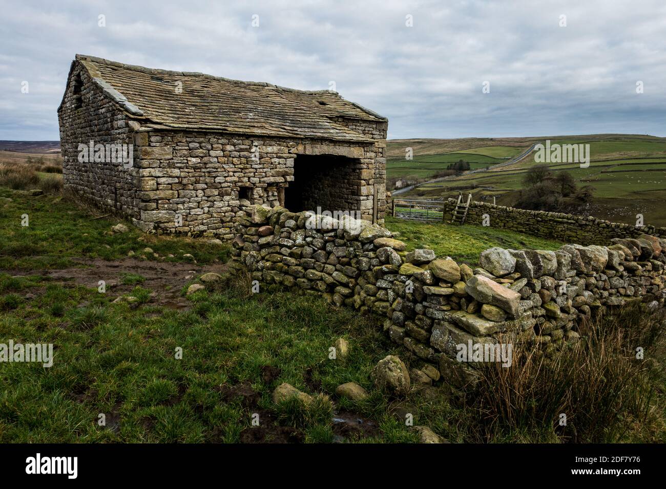 Vecchio fienile di pietra con stile di legno e la B6265 sullo sfondo vicino a Hebden e Burnsall, Yorkshire Dales National Park, North Yorkshire, Eng Foto Stock