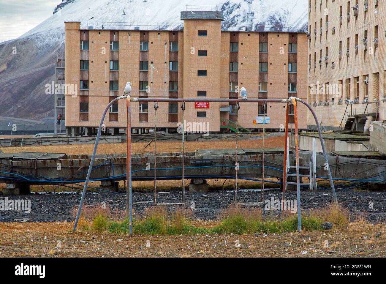 Hotel Tulpan e vecchio swing sul parco giochi per bambini a Pyramiden, abbandonato insediamento sovietico di miniere di carbone su Svalbard / Spitsbergen Foto Stock