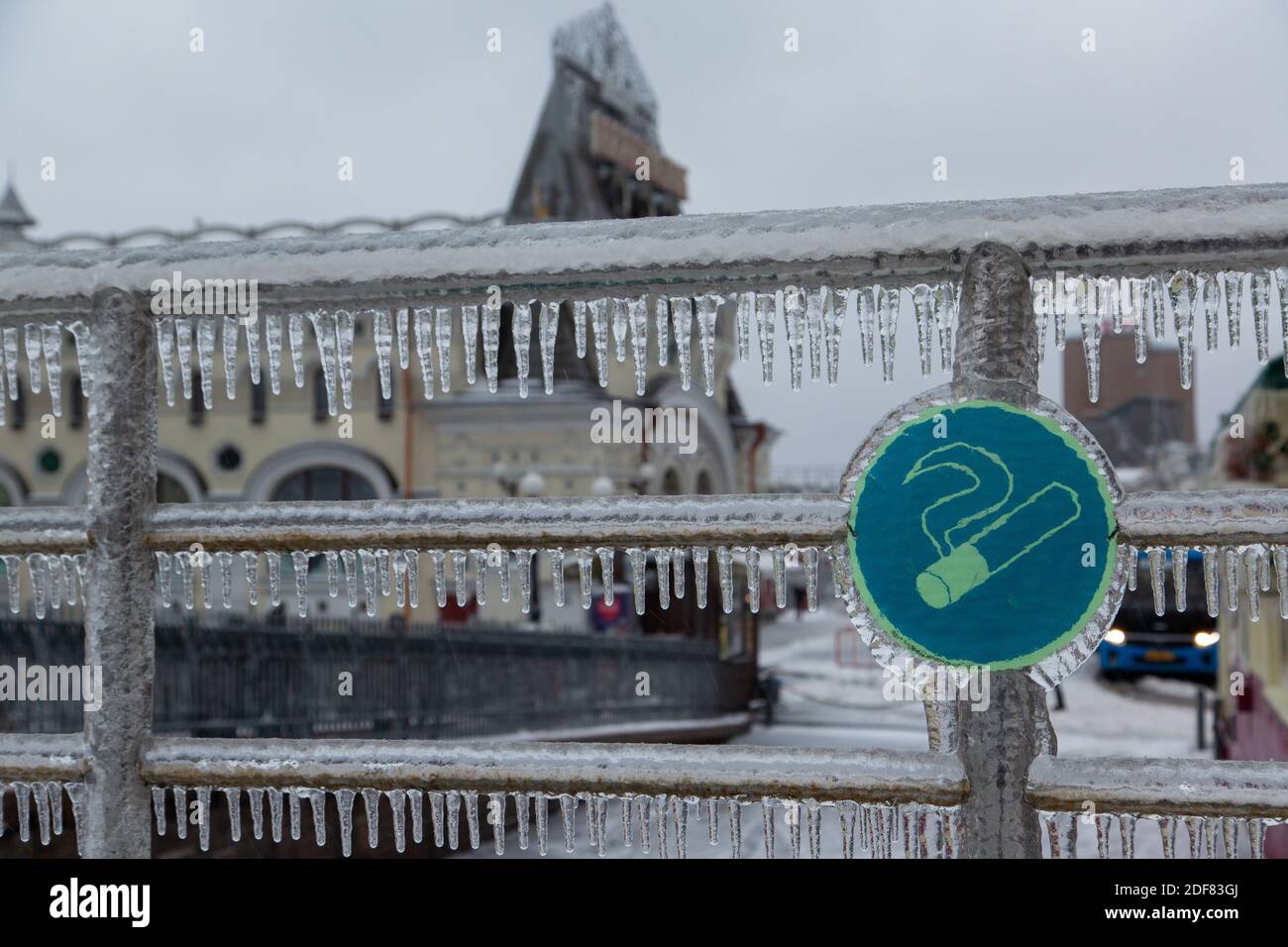Cartello non fumatori appeso su ringhiere in acciaio cromate in città. Le ringhiere sono molto ghiacciate, i icicles appendono giù. Foto Stock