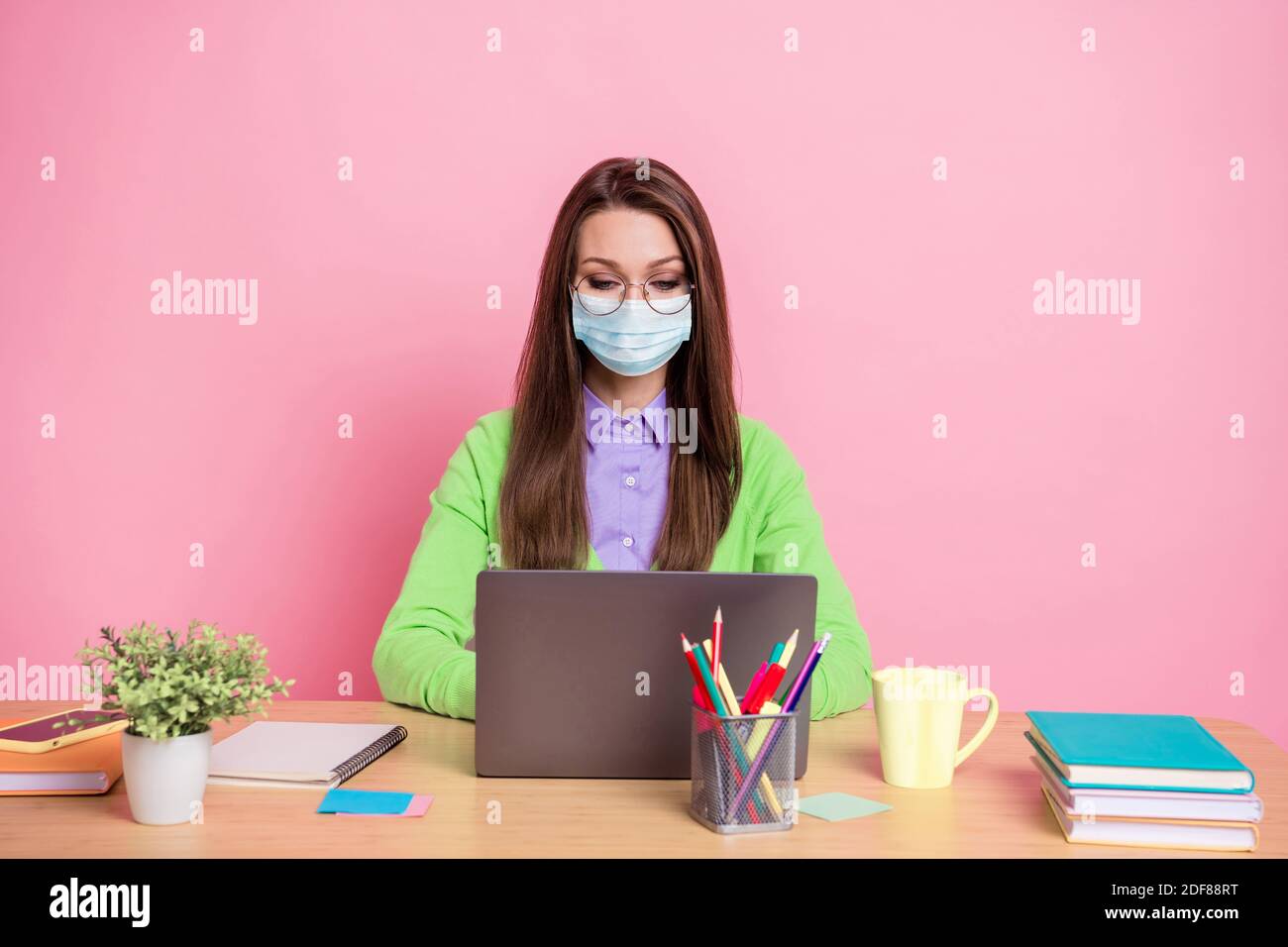 Ritratto di ragazza messa a fuoco sit tavolo lavoro portatile a distanza camicia verde maschera medica isolato colore pastello sfondo Foto Stock