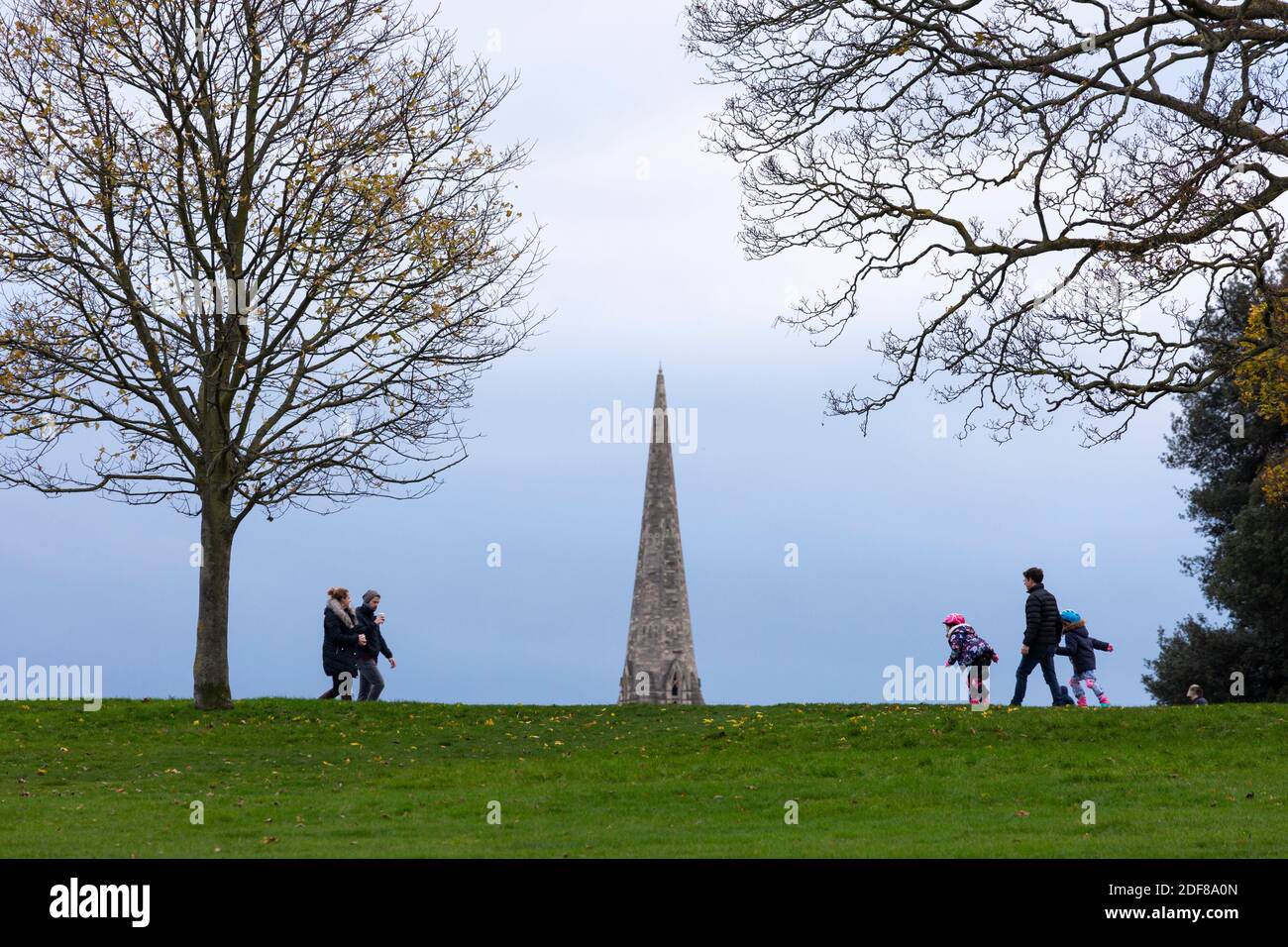 Persone che camminano nel Brockwell Park con il campanile della Santa Trinità Chiesa sullo sfondo, Londra Foto Stock