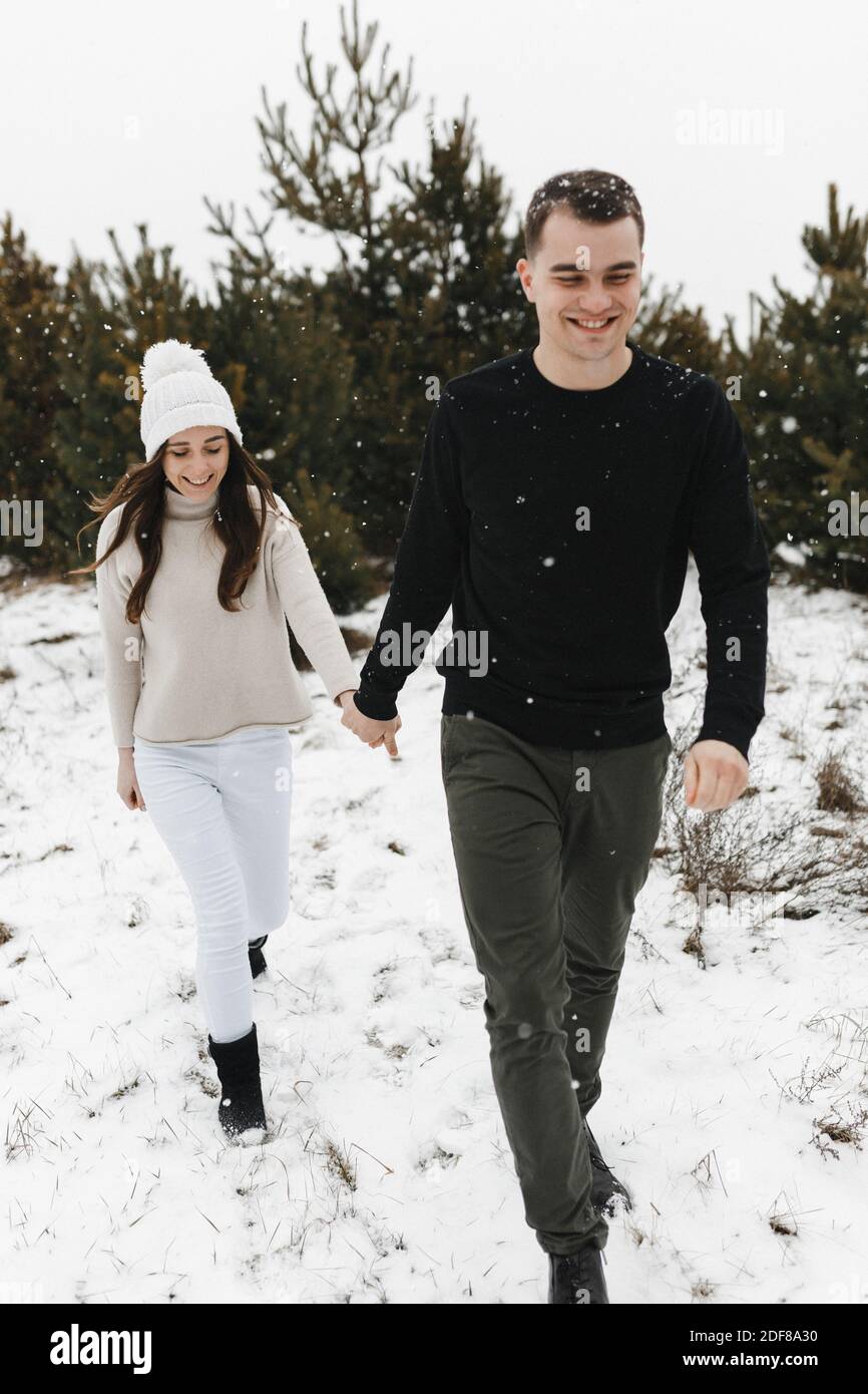 Giovane uomo e donna che si innevano nella pineta tenendolo per le mani. Amore, rapporto, vacanze invernali. Idee di foto di coppia di inverno Foto Stock