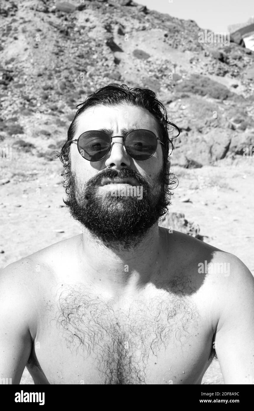il giovane uomo con i capelli bagnati dopo un bagno sulla spiaggia indossa occhiali da sole in stile informale Foto Stock