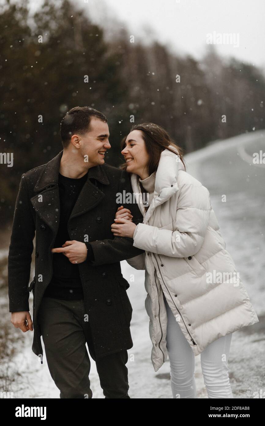 Giovane e donna che si snoda lungo la strada invernale e si sorride l'un l'altro. Amore, rapporto, vacanze invernali. Idee di foto di coppia di inverno Foto Stock