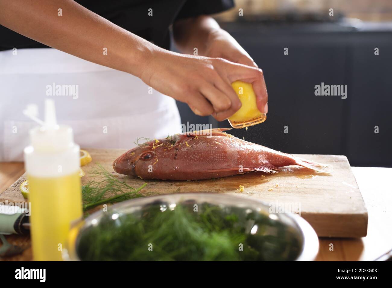 Metà sezione dello chef grattugiare la scorza di limone sul pesce arrosto in cucina ristorante Foto Stock