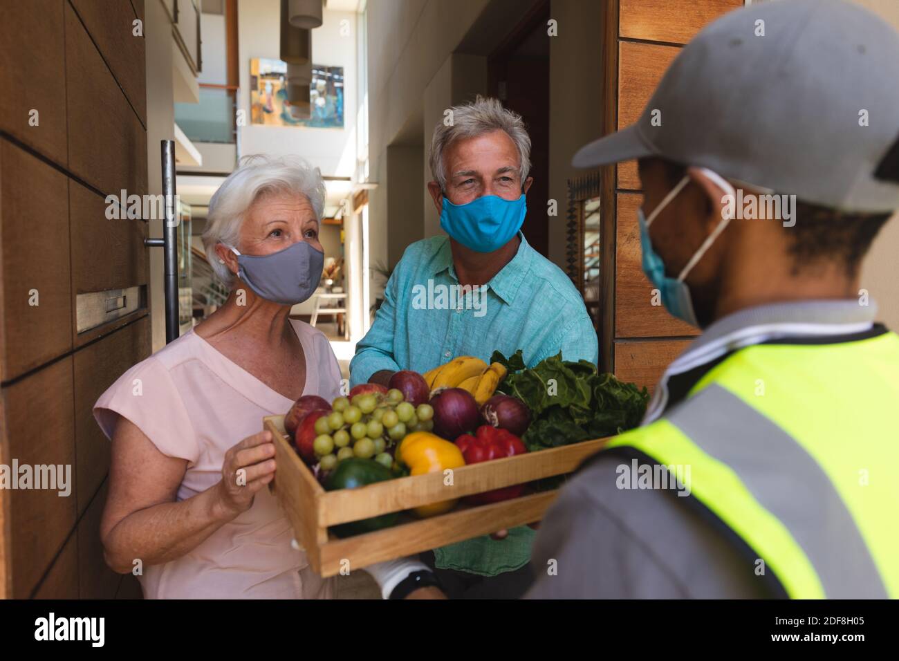 Coppia caucasica superiore che indossa maschere facciali che ricevono consegna di cassa di frutta Foto Stock