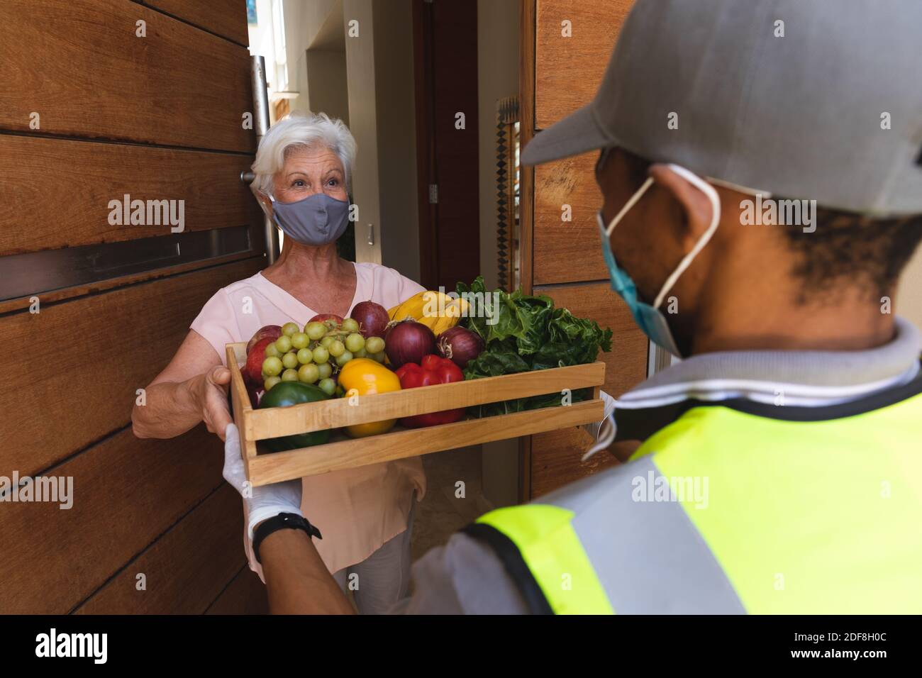 Donna caucasica anziana che indossa la maschera facciale che riceve la consegna della cassa di frutta Foto Stock