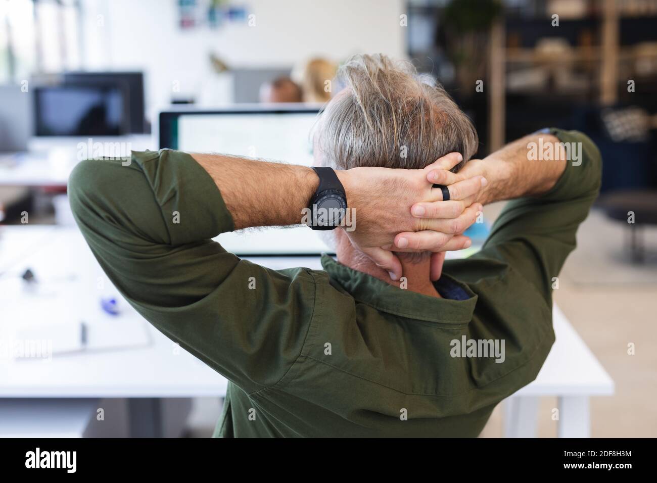 Vista posteriore dell'uomo caucasico in ufficio creativo che riposa, mani sulla testa Foto Stock