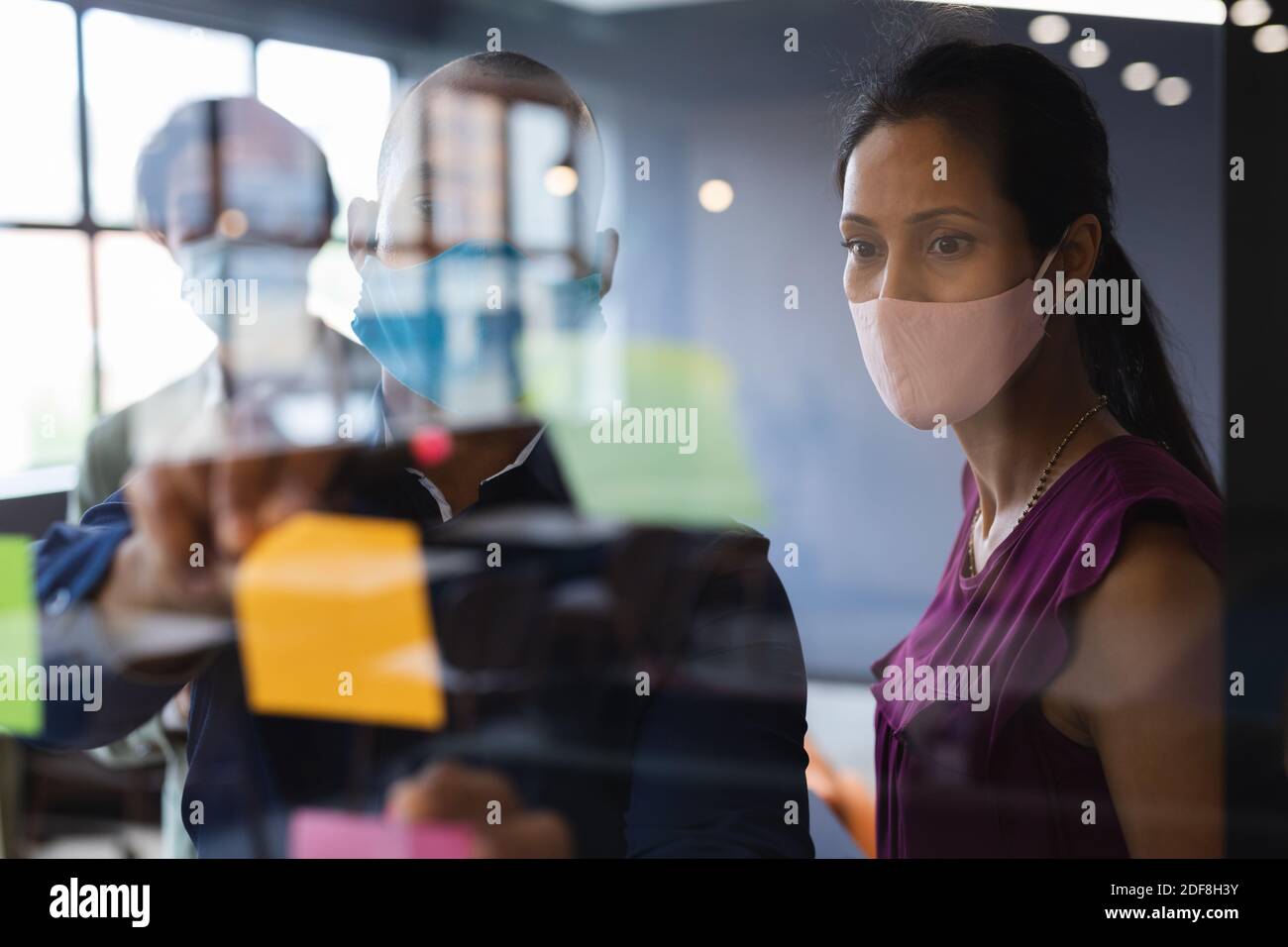 Diverse persone di affari che indossano maschere di scrittura sulla tavola di vetro in ufficio Foto Stock