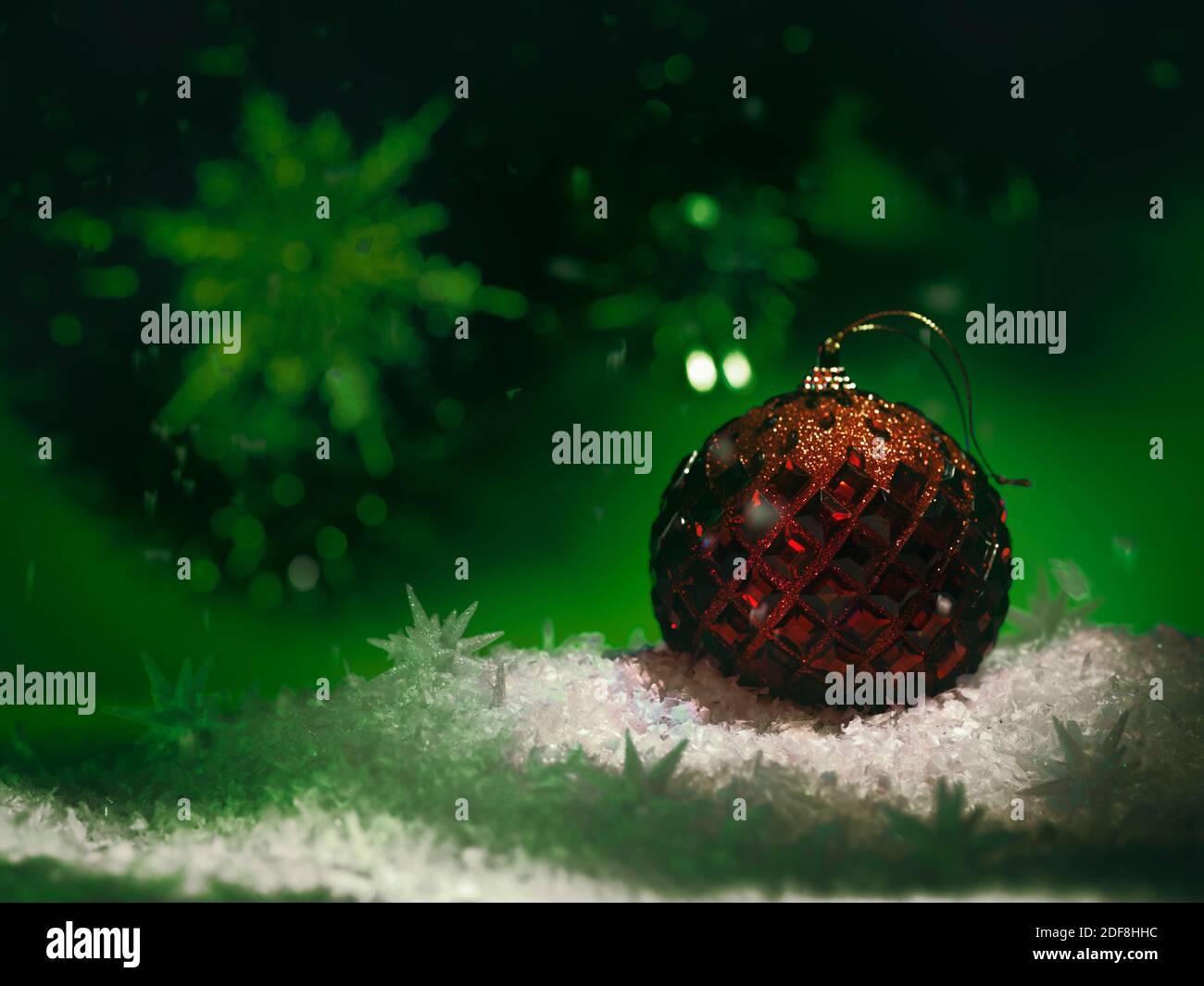 Ornamento di Natale rosso su sfondo verde con neve bianca in ambienti bui. Vacanze invernali artistiche, concetto di nuovo anno. Foto Stock