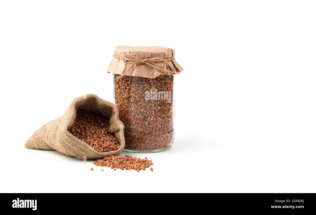 Grano saraceno in un vaso di vetro e in un sacchetto, sparso sul tavolo su uno sfondo bianco. Vista laterale con spazio per la copia. Foto Stock