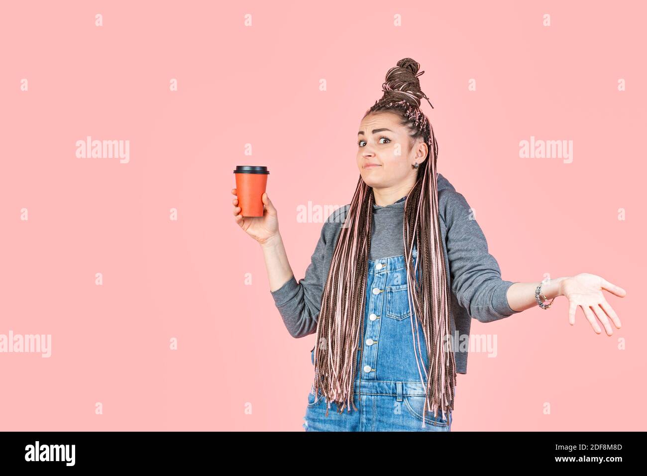 Elegante bella donna giovane con afro pigtail contiene una tazza di caffè di carta usa e getta. Sorpresa su viso e braccia sparse. Concetto per la pubblicità bevanda Foto Stock