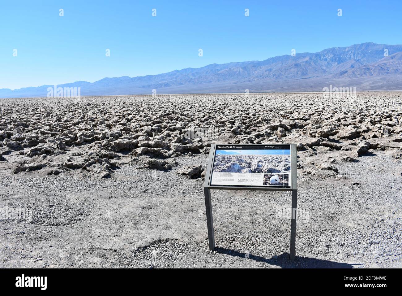 Campo da golf Devils con la catena montuosa Armargosa dietro nel Parco Nazionale della Death Valley. Un segno per i visitatori si trova vicino alle formazioni di cristallo di sale. Foto Stock
